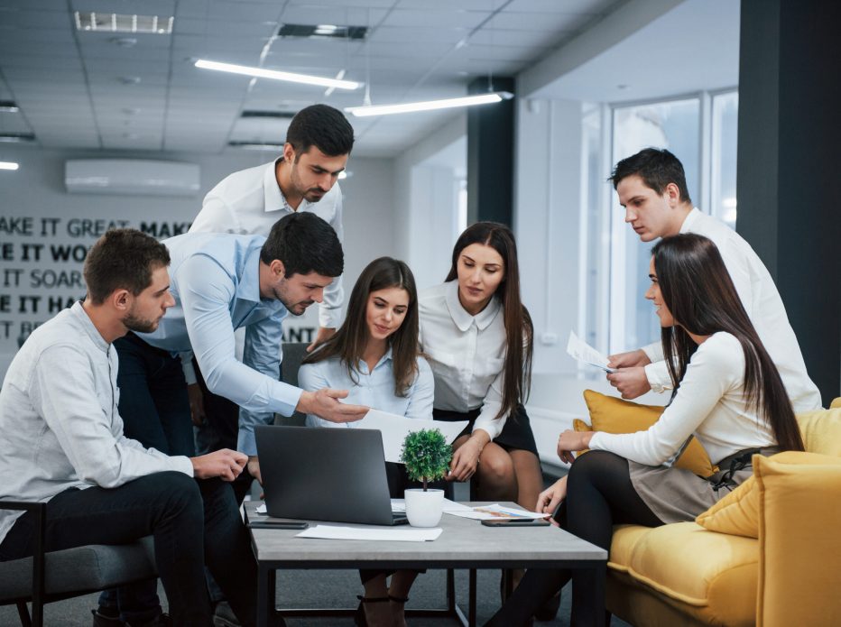 Guy shows document to a girl. Group of young freelancers in the office have conversation and working.